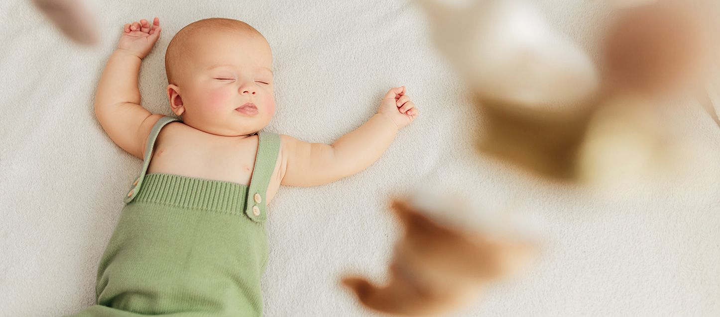 bebe con pijama de tirantes verde durmiendo plácidamente sobre la cama