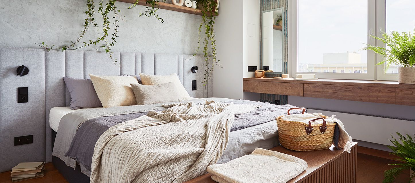 dormitorio de un apartamento pequeño con cama, edredon, cojines, cabecero y mesa de madera