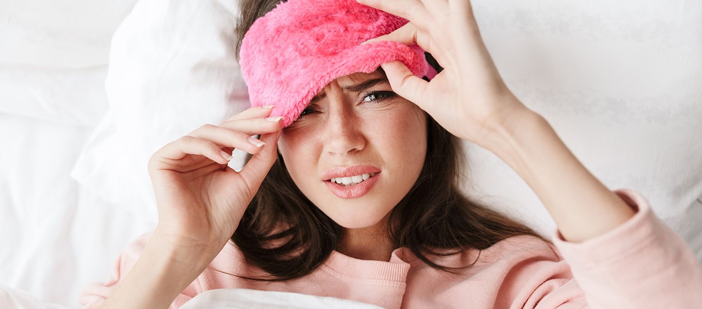 mujer metida en la cama con pijama rosa y antifaz rosa mirando de frente con trastorno en la conducta del sueño