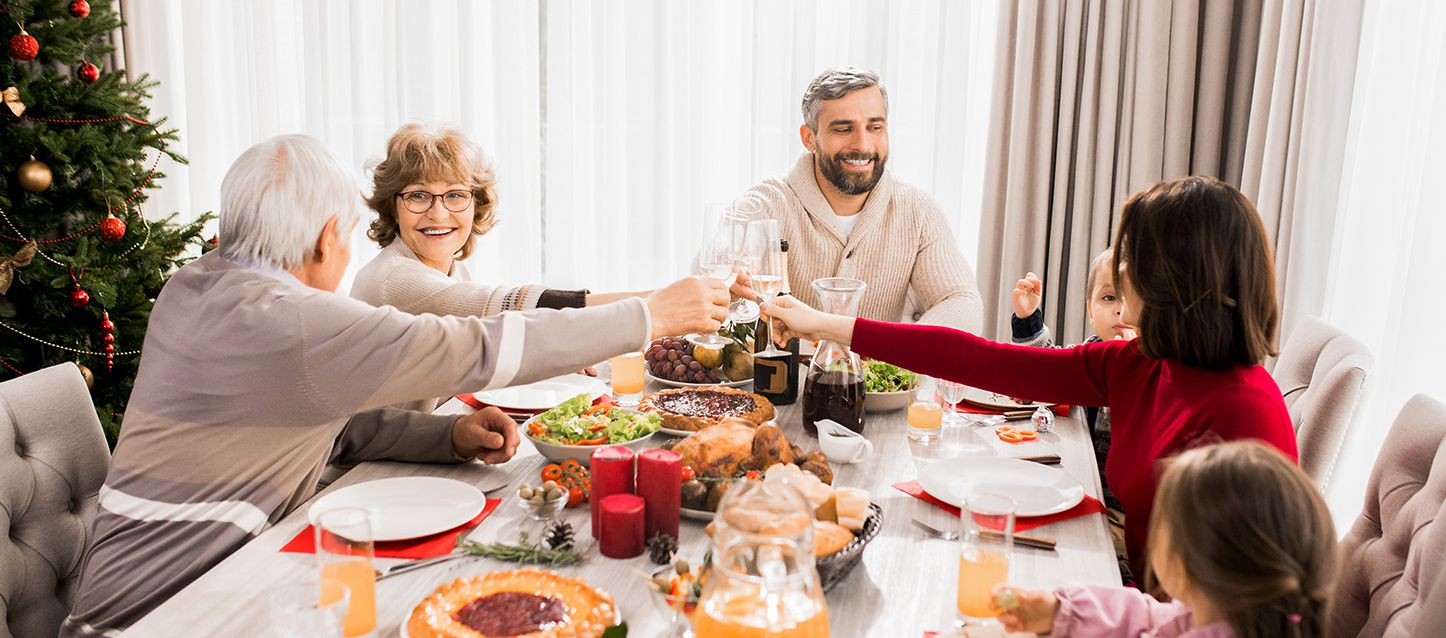 Familia de 2 abuelos, 2 padres y dos niños pequeños comiendo sentados juntos en una mesa con varios platos de comida, velas y vino