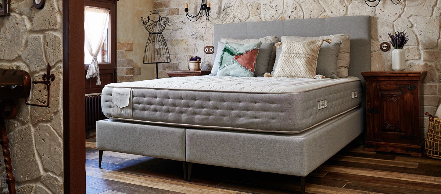 Base y colchón de maxcolchon con cojines y almohadas apoyadas en el cabecero de la cama en una habitación con el suelo de madera